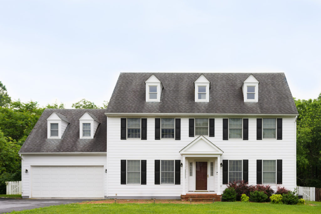 A beautiful white and grey home surrounded by green trees under a clear sky